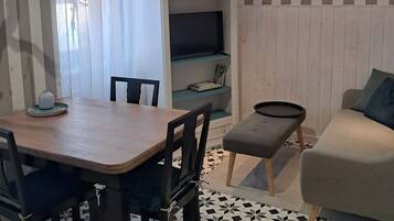 A room with a dining table, chairs, a sofa, a TV, and a patterned floor.
