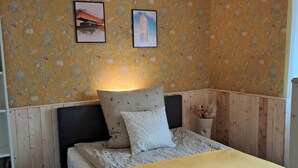 Ein Schlafzimmer mit einem Bett, einem Nachttisch, einer Wandlampe und zwei gerahmten Bildern.