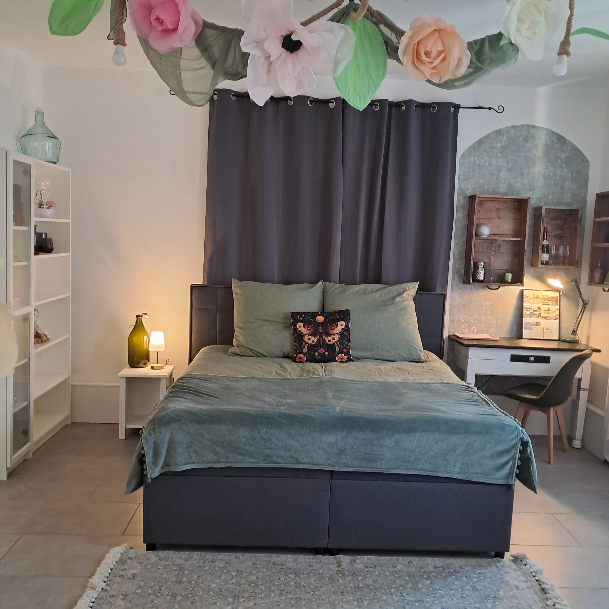 A bedroom with a bed, a desk, and a shelving unit.