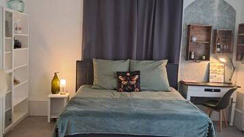 A bedroom with a bed, a desk, and a shelving unit.