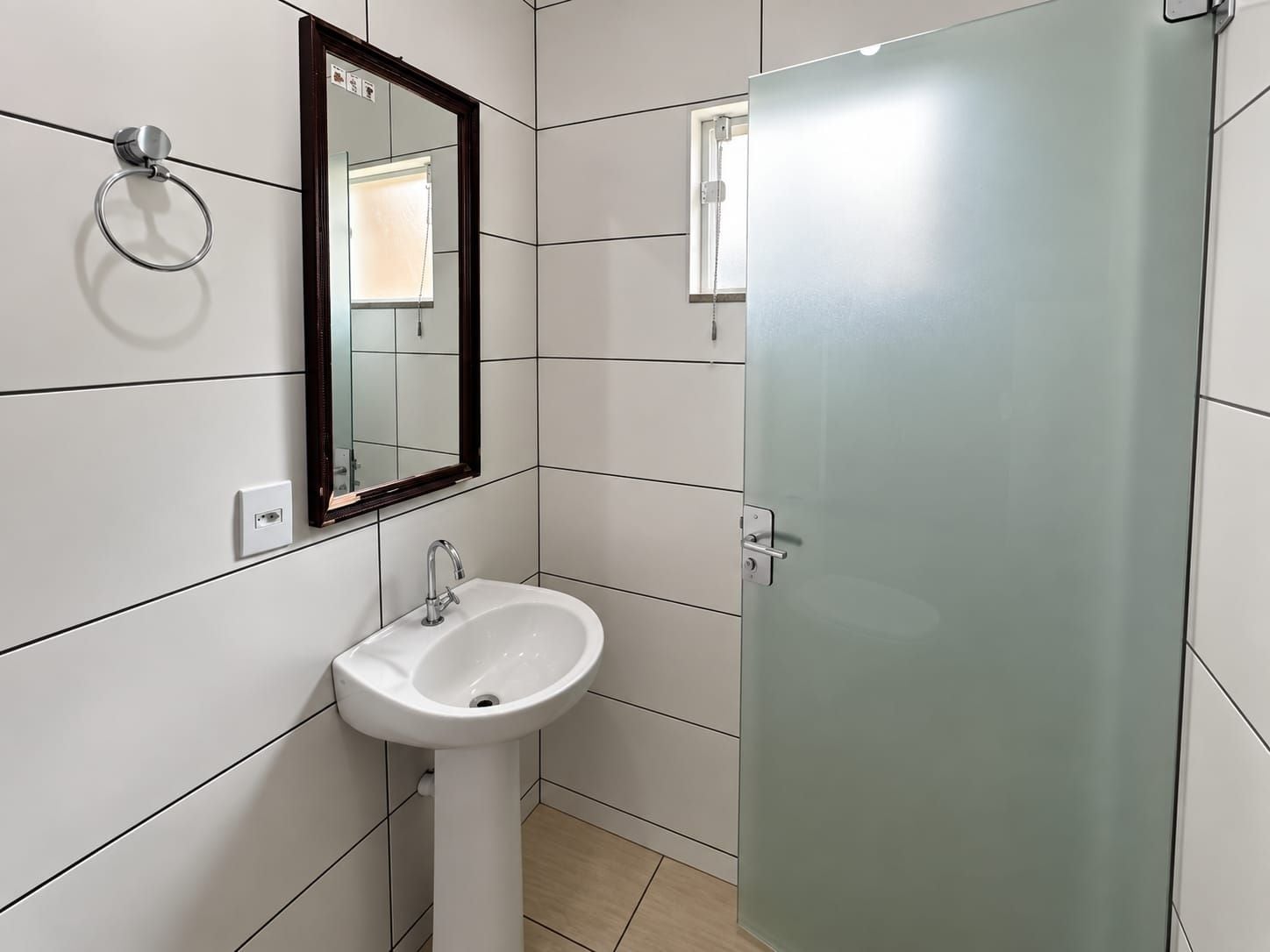 Un ba ño con lavamanos blanco, un espejo y mampara de vidrio.