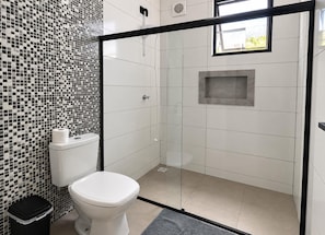 A modern bathroom with a toilet, a shower enclosure, and a mosaic tile wall.