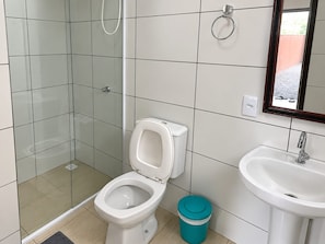 A bathroom with a toilet, a sink, and a shower. - Pousada Tio Tonho (Penha)