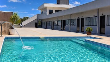 A modern hotel with a swimming pool, a covered outdoor area, and a car parked nearby.