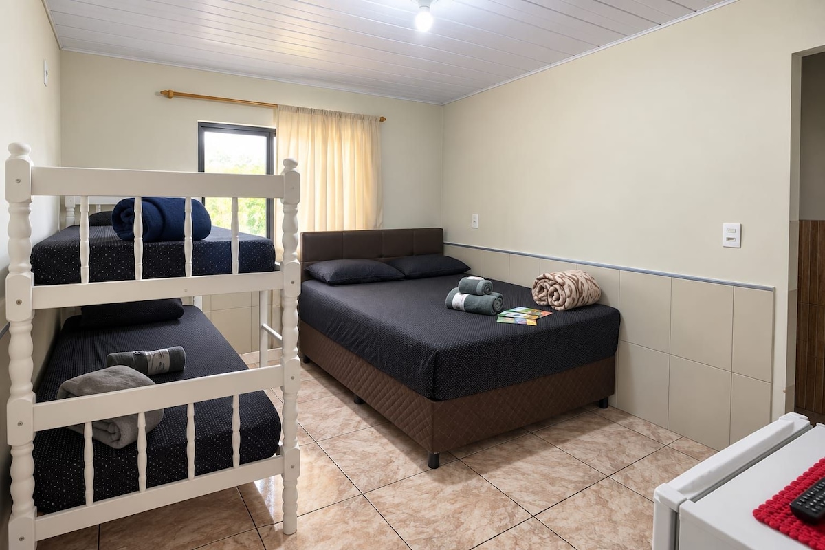 Ein Zimmer mit einem Etagenbett, einem Einzelbett und einem kleinen Tisch mit einer Fernbedienung.