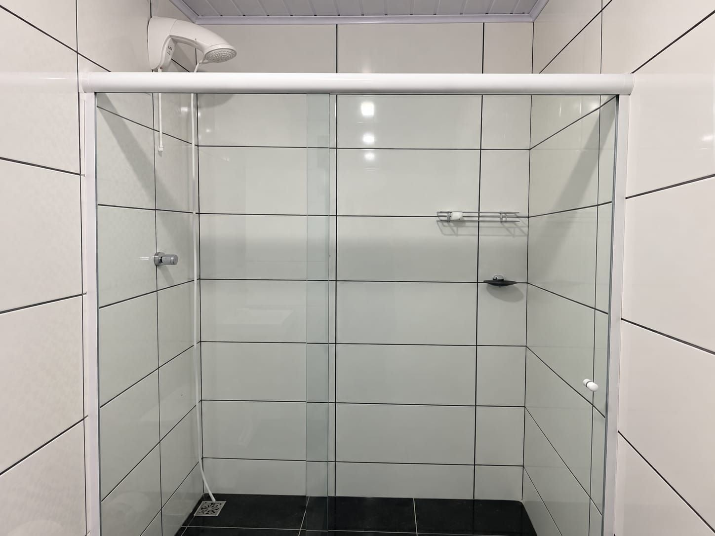 Een douchecabine met een glazen deur, een wit plafond en een zwarte vloer.