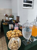 Una mesa de buffet con diversos alimentos, como pan, pasteles y un dispensador de bebidas.