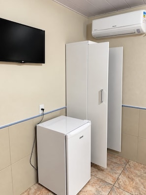 A small room with a flat-screen TV mounted on the wall, a white mini-fridge, and a white cabinet with a door. - Pousada Tio Tonho (Penha)