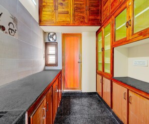A kitchen with wooden cabinets, a black countertop, and a tiled backsplash. - Super Deluxe Room (Tirupati)