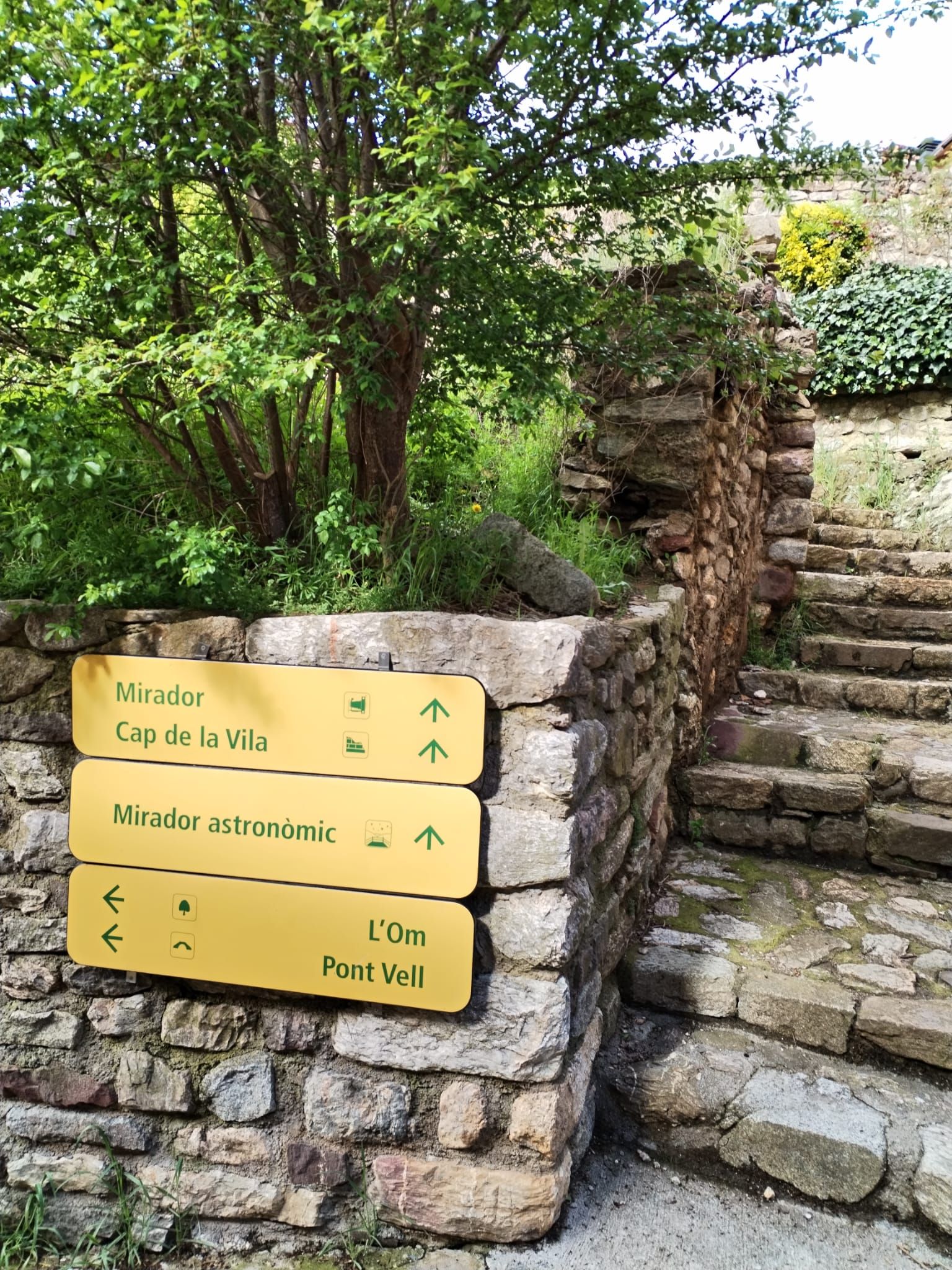 Un escalier en pierre mène à un panneau indiquant différentes directions à l’aide de flèches et de texte, et précisant l’emplacement de divers points de vue.