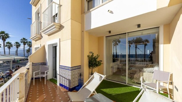 A balcony with white lounge chairs, a small table, and a glass door leading to a covered outdoor area. - Vrbo Property (Almería)