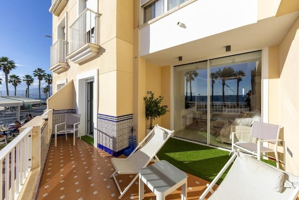 Ein Balkon mit weißen Lounge-Stühlen, einem kleinen Tisch und einer Glasdoor zu einem überdachten Außenbereich.