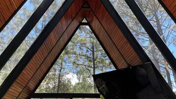 Une structure triangulaire en bois formant un plafond, avec une fenêtre en verre à la base, qui offre une vue sur une zone boisée.