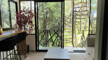 Un intérieur moderne avec un sol en marbre, un plafond en bois, un coin repas comprenant des chaises et une table, et une grande porte-fenêtre coulissante donnant sur un balcon avec vue sur les arbres.