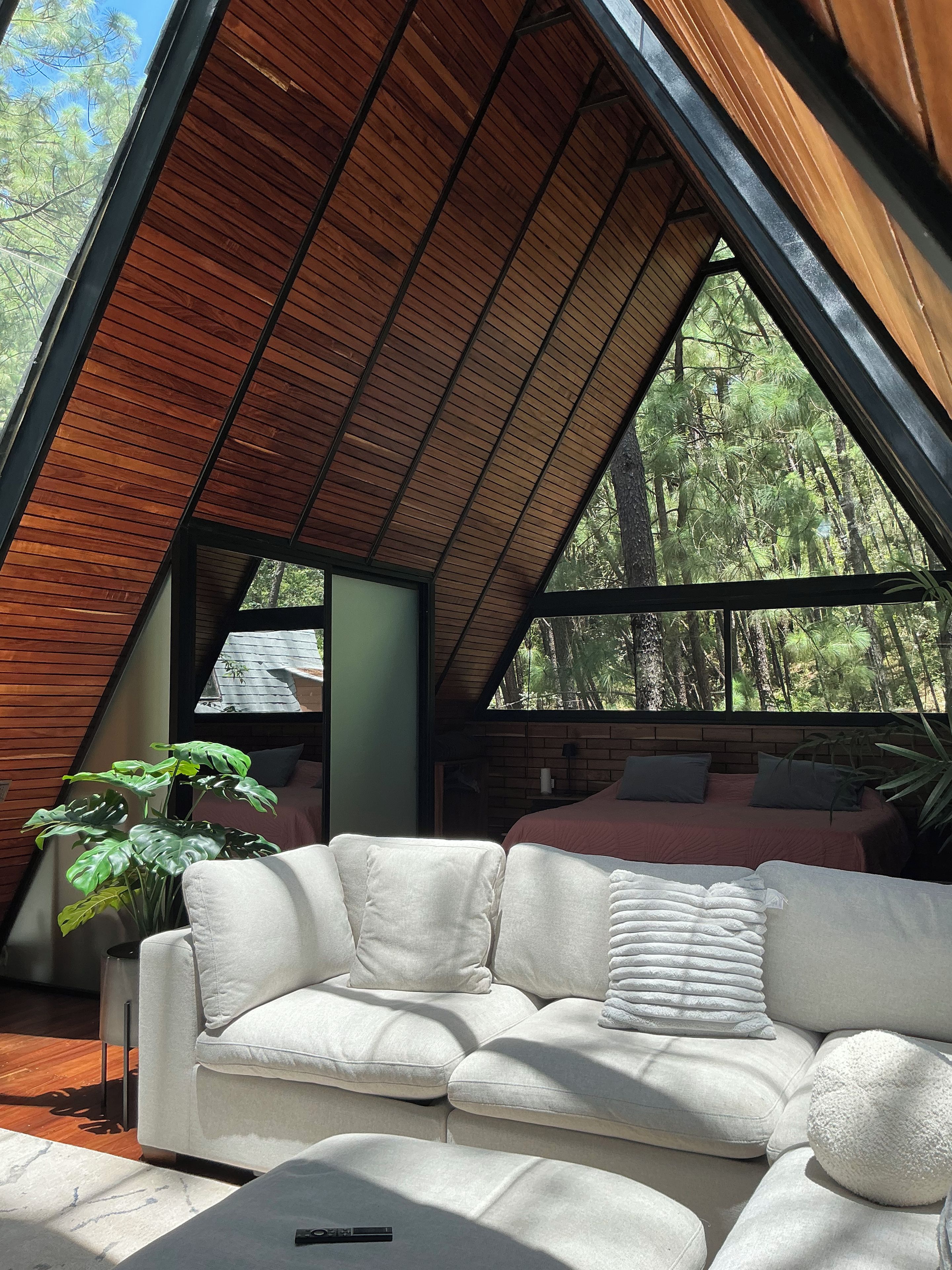 A modern interior with a sloped ceiling, a white sofa, and a large window offering a view of a forest.