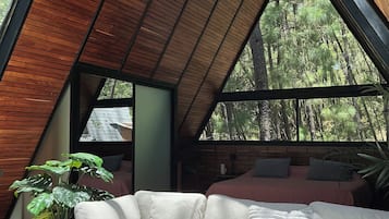 A modern interior with a sloped ceiling, a white sofa, and a large window offering a view of a forest.
