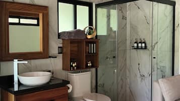 A modern bathroom with a wooden vanity, a large mirror, a white toilet, a glass shower enclosure, and a beige sofa.