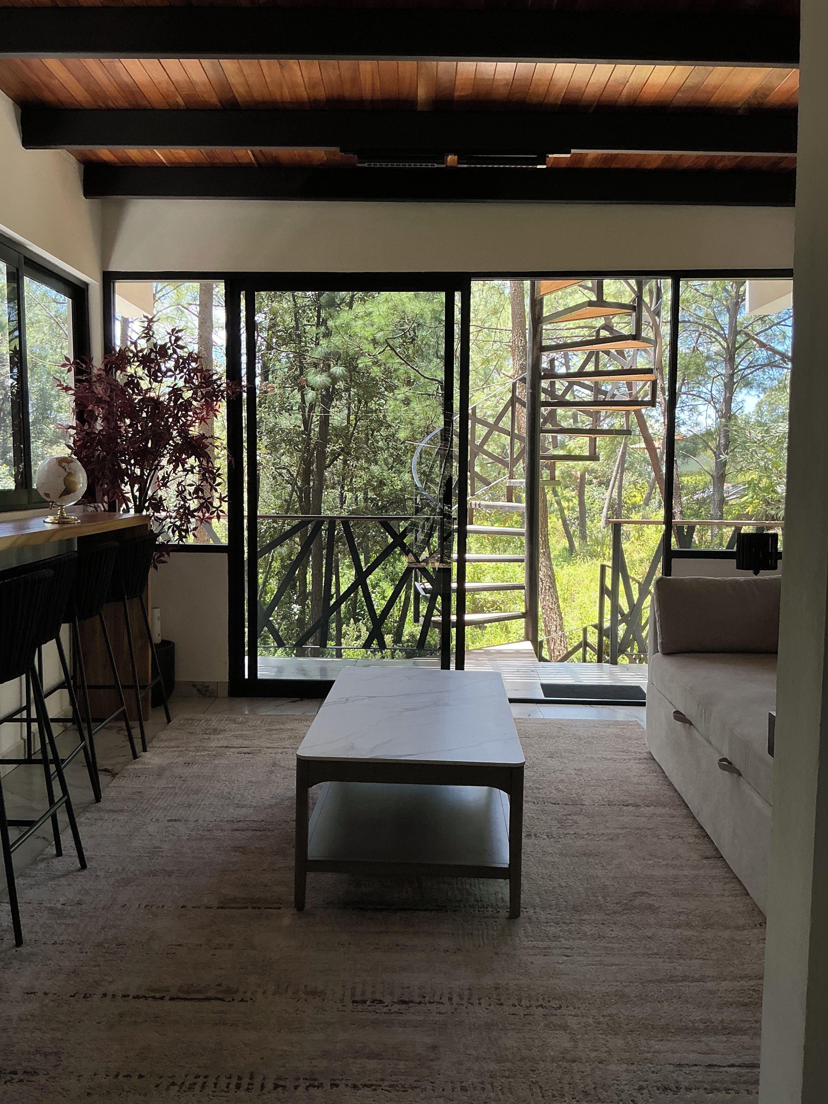 Un intérieur moderne avec une grande porte-fenêtre coulissante donnant sur un balcon, une table surmontée d’un plateau en marbre et un coin bar avec des tabourets.