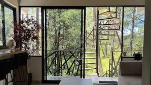 Un intérieur moderne avec une grande porte-fenêtre coulissante donnant sur un balcon, une table surmontée d’un plateau en marbre et un coin bar avec des tabourets.