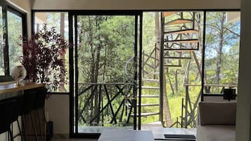 Un intérieur moderne avec une grande porte-fenêtre coulissante donnant sur un balcon, une table surmontée d’un plateau en marbre et un coin bar avec des tabourets.