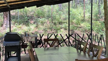 Un espace de restauration extérieur abrité, avec une table et des chaises, un barbecue et une vue sur une zone boisée.