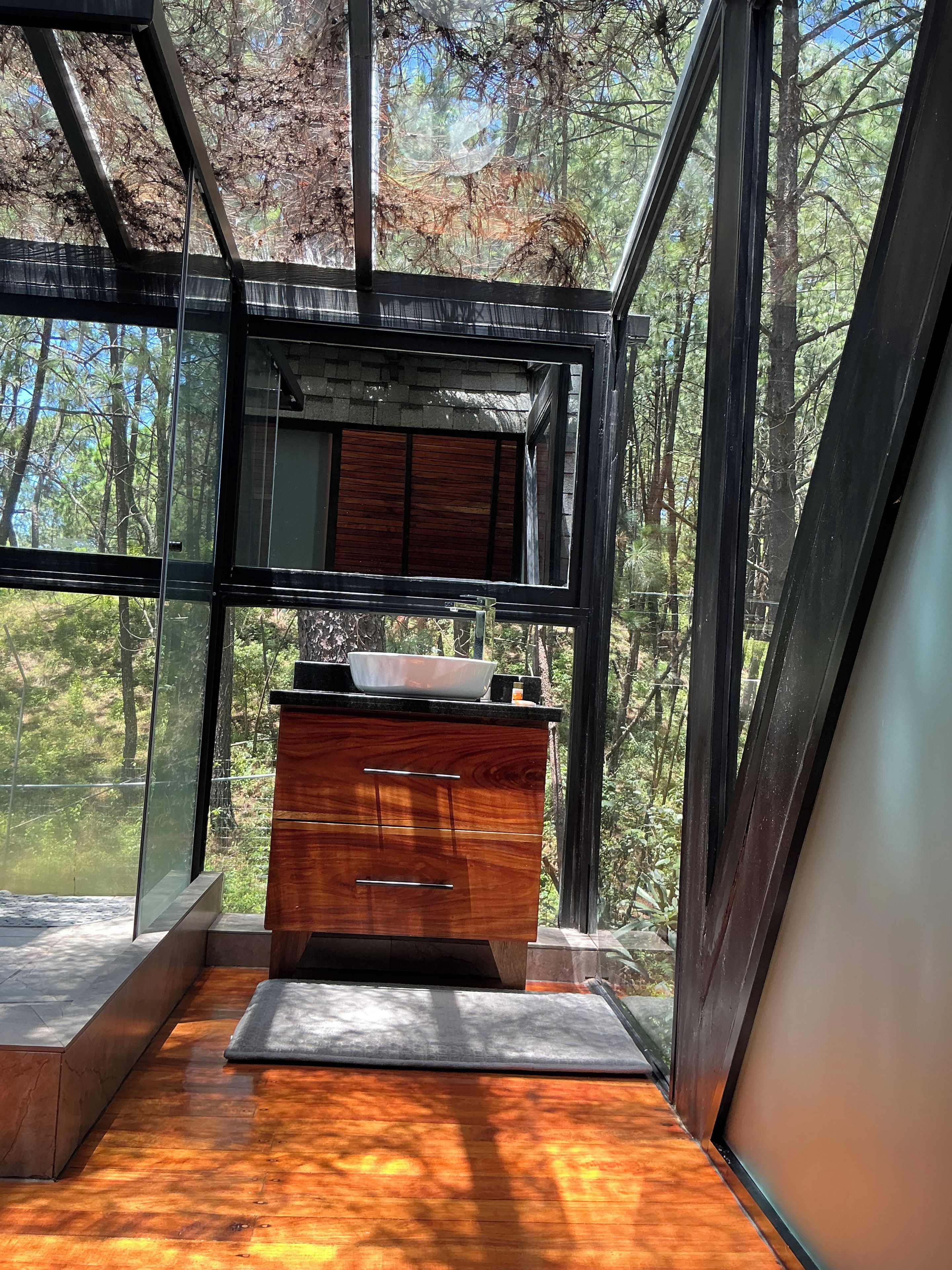 A modern bathroom with a wooden vanity and a large window offering a forest view.