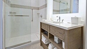 A modern bathroom with a glass-enclosed shower, a wooden vanity with a mirror, and a white countertop. - Studio Deluxe, Ocean View, at Wyndham Rio Mar in Puerto Rico, on Golf Course! (Río Grande)