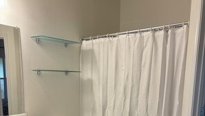 Un baño con inodoro, repisa de vidrio, cortina de ducha y alfombra azul oscuro.