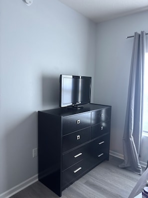 Een zwarte dressoir met een televisie erboven, een raam met gordijn en een lichtschakelaar aan de muur.