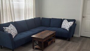 Una sala de estar con un sofá seccional azul oscuro, una mesa de centro de madera y suelo de madera clara.
