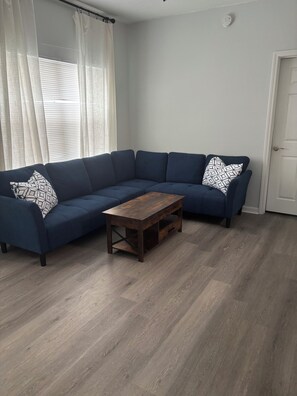 A living room with a dark blue sectional sofa, a wooden coffee table, and light wooden flooring. - 2-bedroom condo on first floor in peaceful Seminole, FL-5 min from Maderia Beach (Seminole)