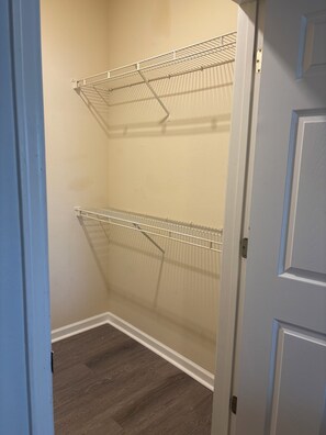 Ein Schrank mit zwei Drahtregalen, einem Holzboden und einer weißen Tür.