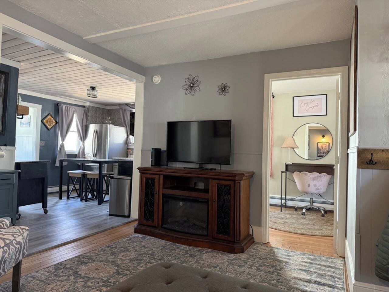 Ein Wohnzimmer mit Fernseher, ein Essbereich mit Tisch und Stühlen sowie eine Küchenzeile mit Schränken und Kühlschrank.