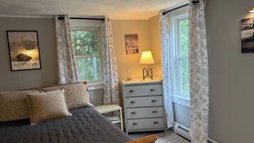 Une chambre à coucher avec un lit, une commode, une lampe et deux fenêtres avec des rideaux.