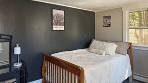 Een slaapkamer met een bed, nachtkastje, lamp en een lijst met een afbeelding aan de muur.