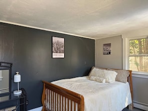 Quarto com cama, mesa de cabeceira, luminária e quadro na parede.