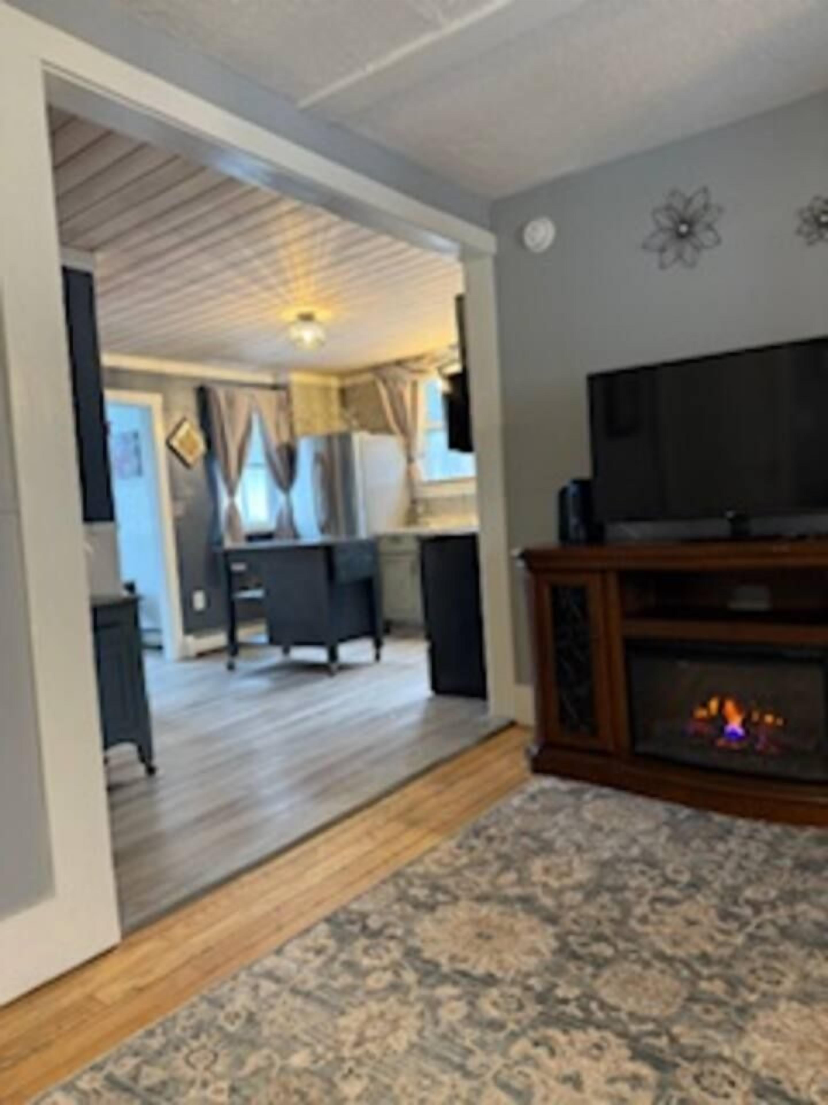 A living room with a fireplace, a television, and a dining area in the background.