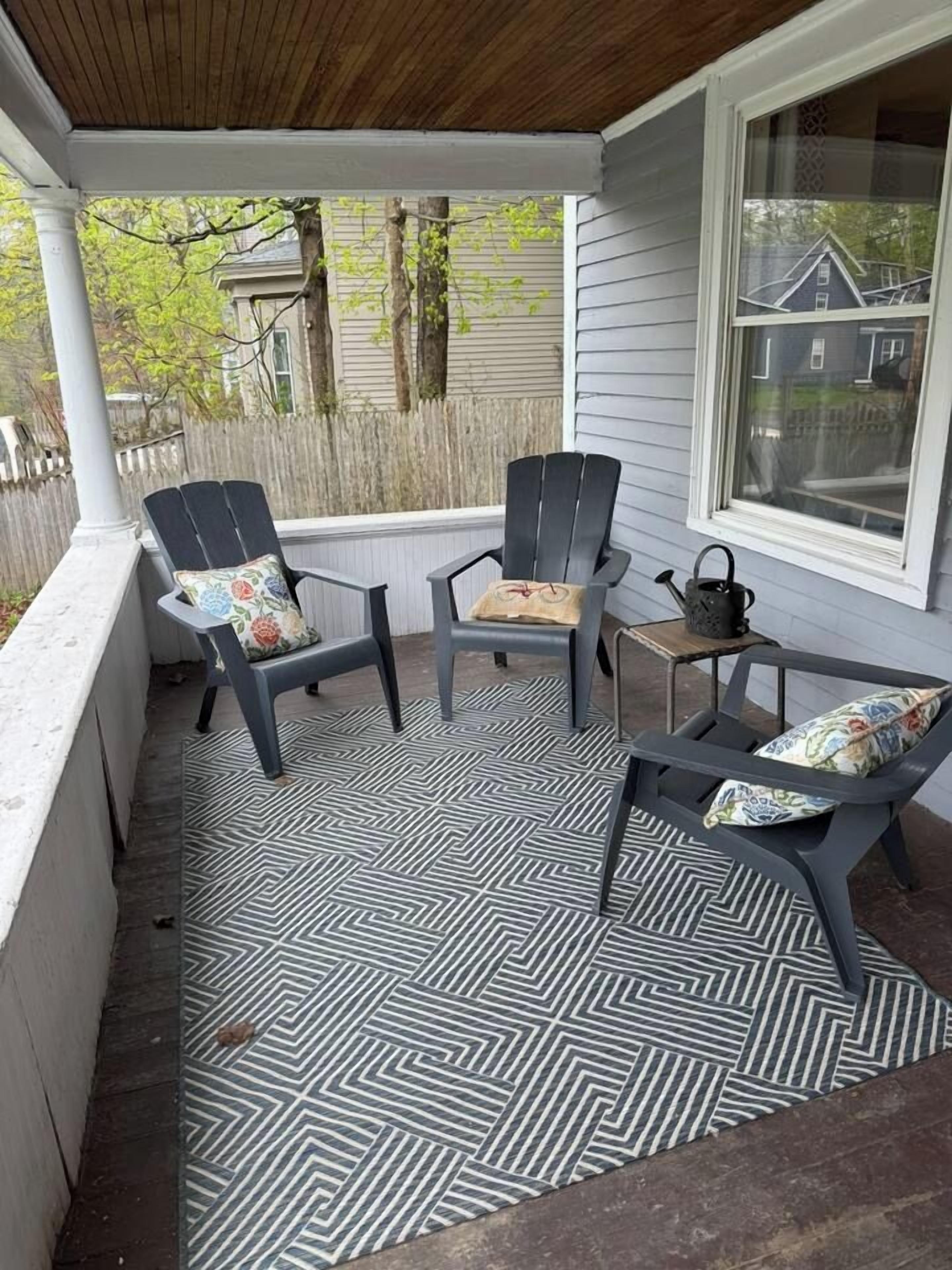 A covered porch with two Adirondack chairs and a small table, featuring a patterned floor.