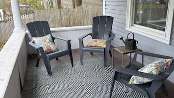 A covered porch with two Adirondack chairs and a small table, featuring a patterned floor.