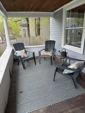 A covered porch with two Adirondack chairs and a small table, featuring a patterned floor.