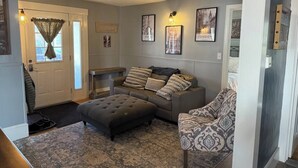 Een woonkamer met een bank, een poef, een kamerkleed met dessin en wanddecoratie.