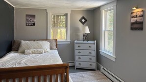 Een slaapkamer met een bed, een dressoir en twee ramen.