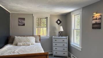 A bedroom with a bed, dresser, and two windows.