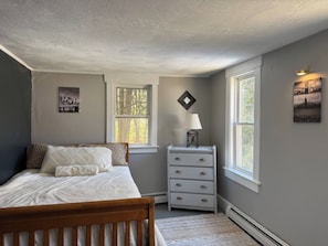 Quarto com cama, cômoda e duas janelas.