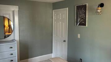 A bedroom with a bed, a dresser, a door, and a wall-mounted light fixture.