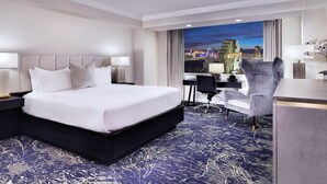 Ein Hotelzimmer mit einem großen Bett, einem Schreibtisch und Blick auf eine beleuchtete Stadt bei Nacht.