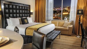 Ein Hotelzimmer mit einem großen Bett, einer Couch, einem Esstisch und Blick auf die beleuchtete Stadt.