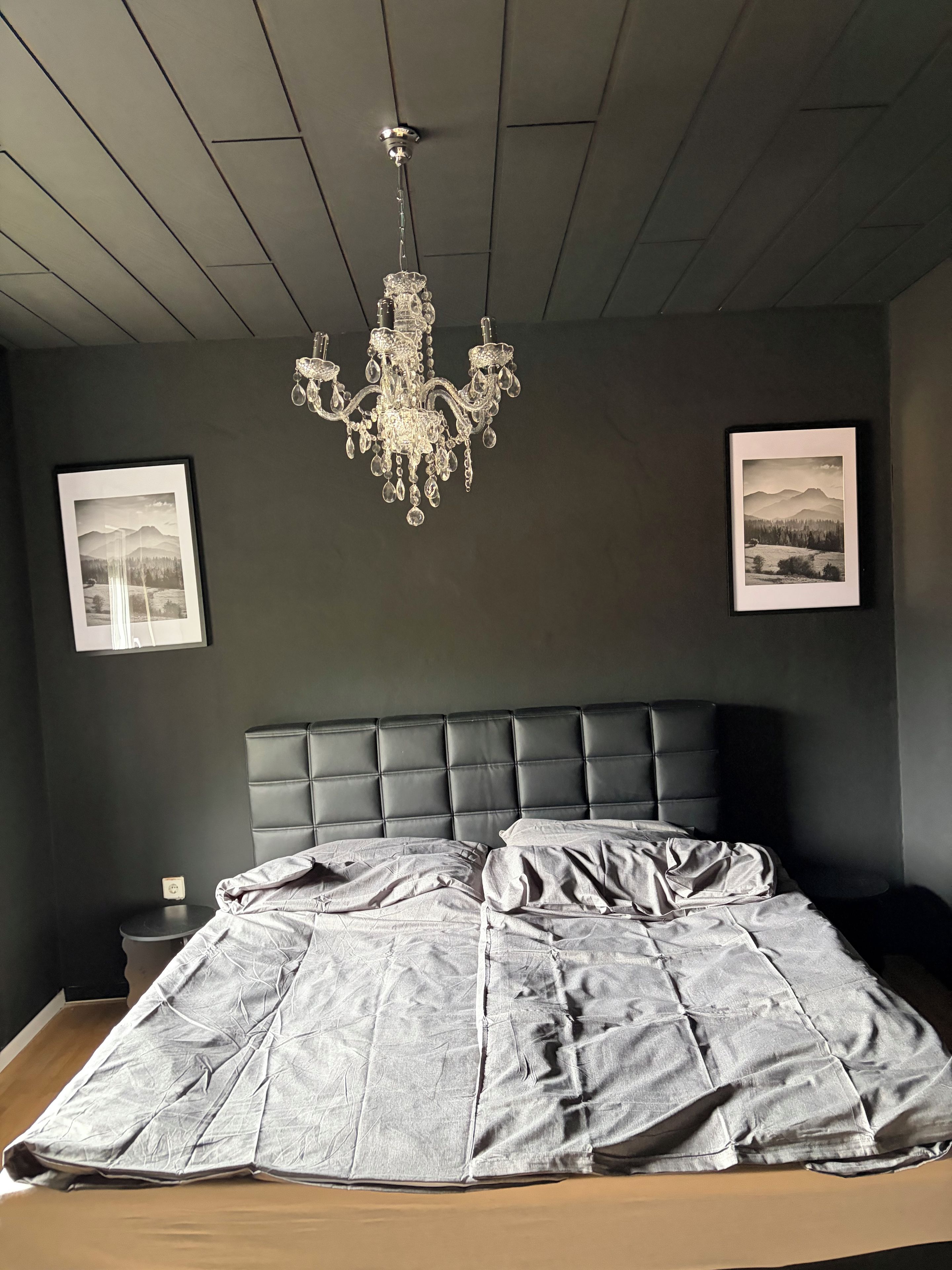 Ein Schlafzimmer mit einem dunkelbraunen Kopfteil, einer Kristallleuchtre und zwei gerahmten Bildern an der Wand.