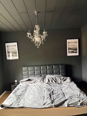 Ein Schlafzimmer mit einem dunkelbraunen Kopfteil, einer Kristallleuchtre und zwei gerahmten Bildern an der Wand.