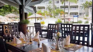 Ein Restaurant mit gedeckten Tischen, Sonnenschirmen im Freien und Blick auf ein Gebäude mit Balkonen.